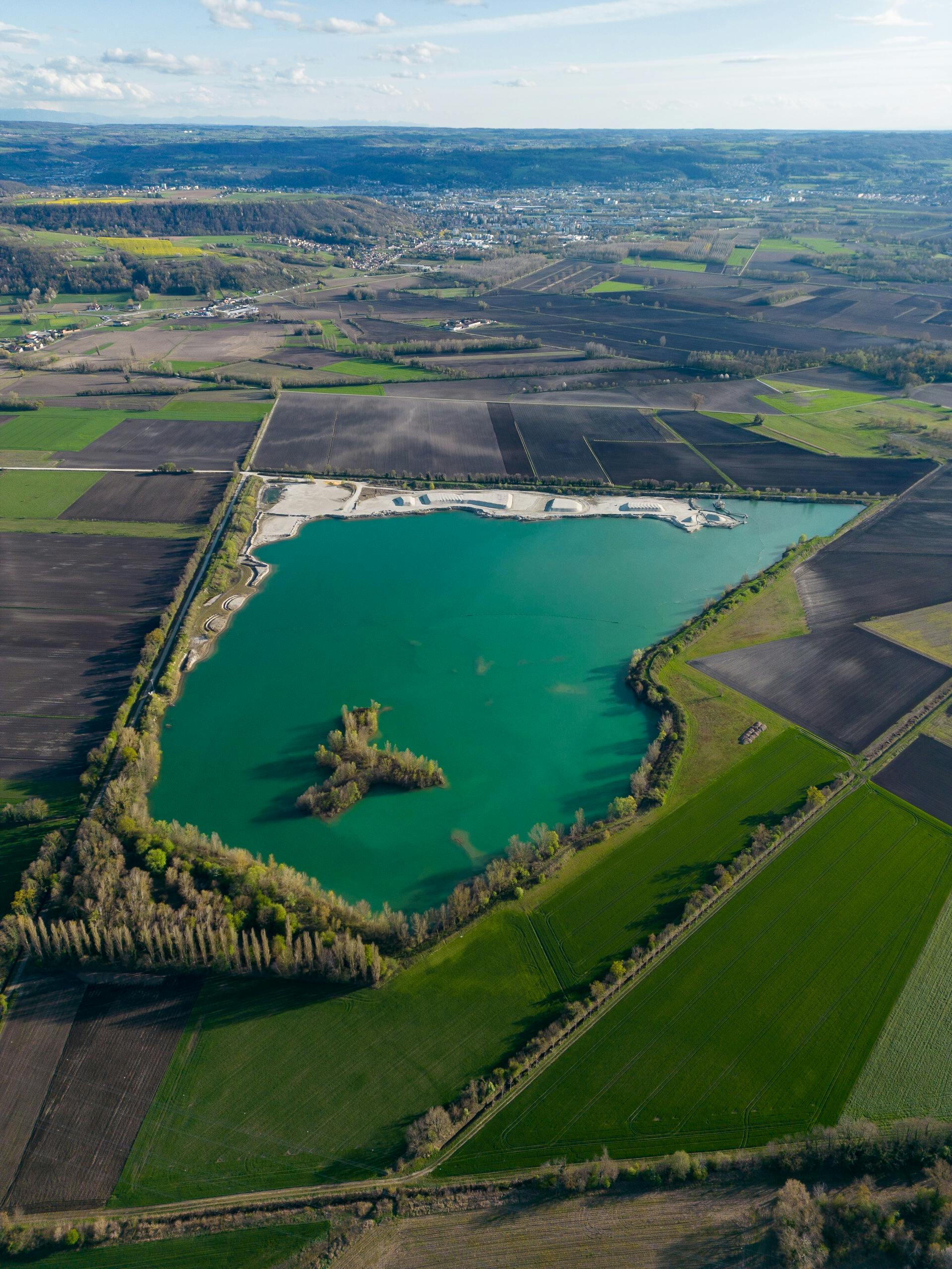 Discover the stunning landscape of Bourgoin-Jallieu, France with this aerial shot of a pristine lake and green fields.